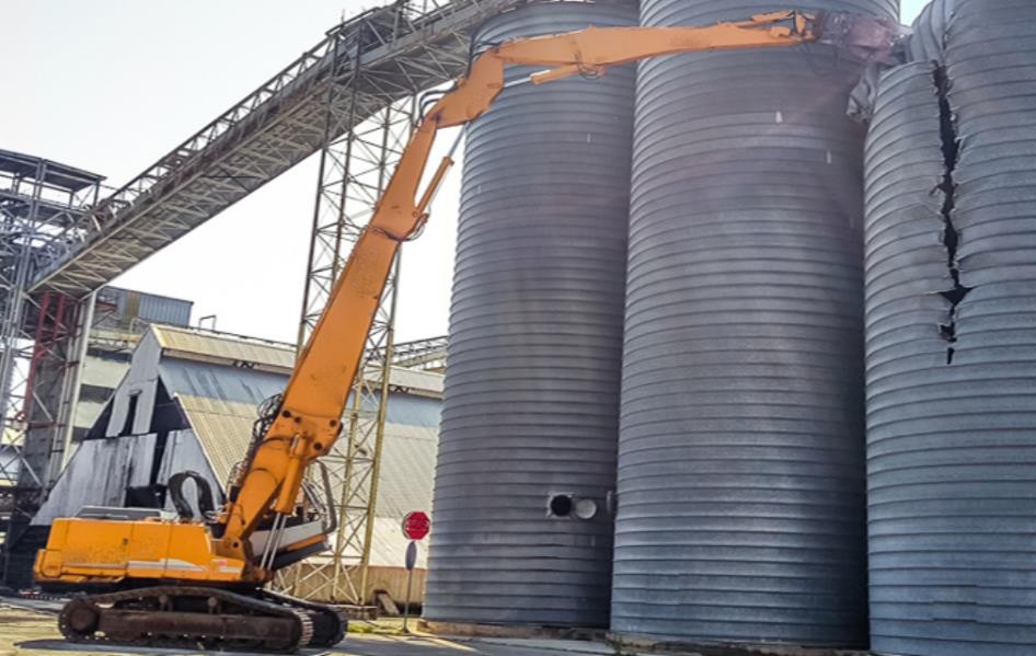 Demolition machine working beside silos